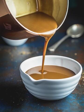 A front on image of caramel sauce being poured from a saucepan in to a white bowl