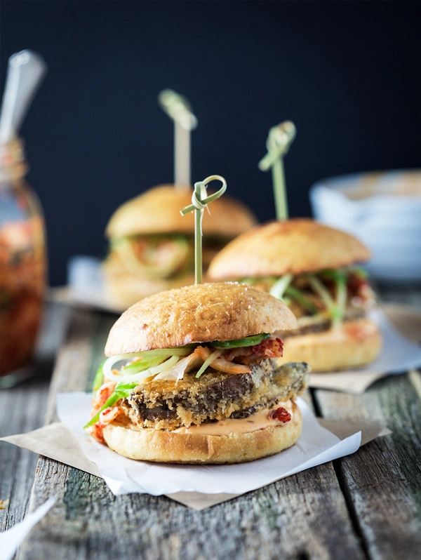 A front on image of a crispy mushroom burgers on a wooden board