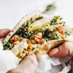 A man's hands holding a stuffed pita in sandwich paper.