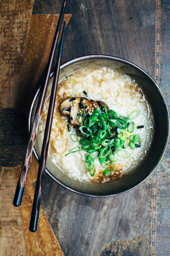 overhead image of a bowl of congee with fried mushrooms and scallions on a rustic wooden table