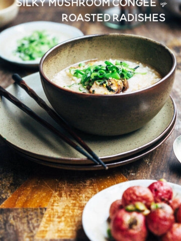 A green bowl of congee with mushrooms and scallions on a wooden table