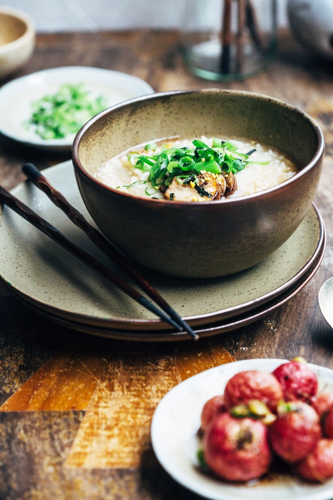 A front-on image of mushroom congee set on a table with a bowl of radishes 