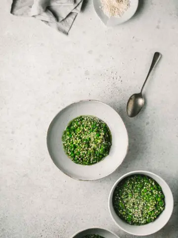 Two bowls of green buckwheat risotto on a grey background