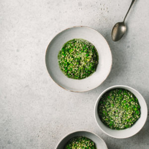 Three bowls of green buckwheat risotto on a grey background