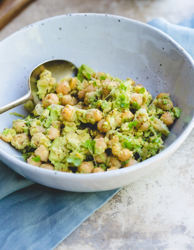 A bowl of the chickpea, sumac and avocado mixture in a white bowl sitting on a concrete bench with a blue napkin nearby