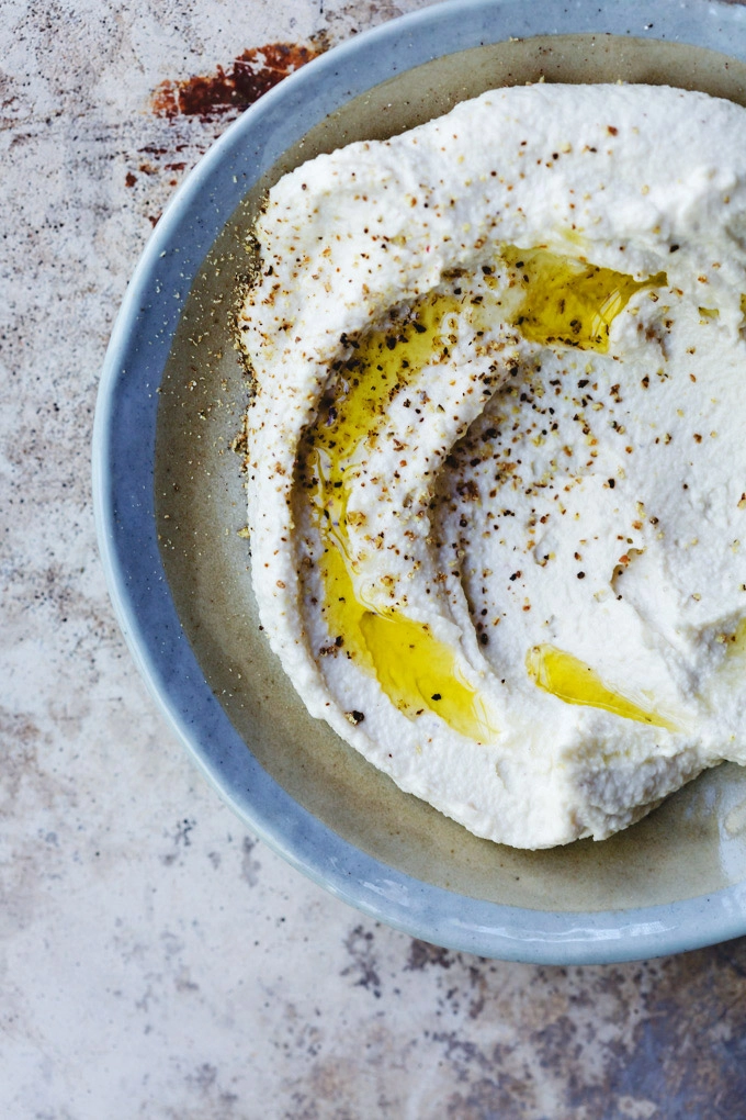 A close-up image of a small plate of cashew cream with a drizzle of olive oil and freshly cracked pepper scattered over