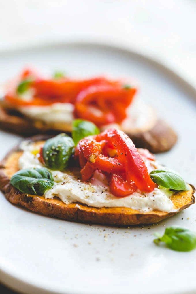 A close-up image of two cashew cream and roast pepper sweet potato toasts serves with baby basil scattered over n a white plate