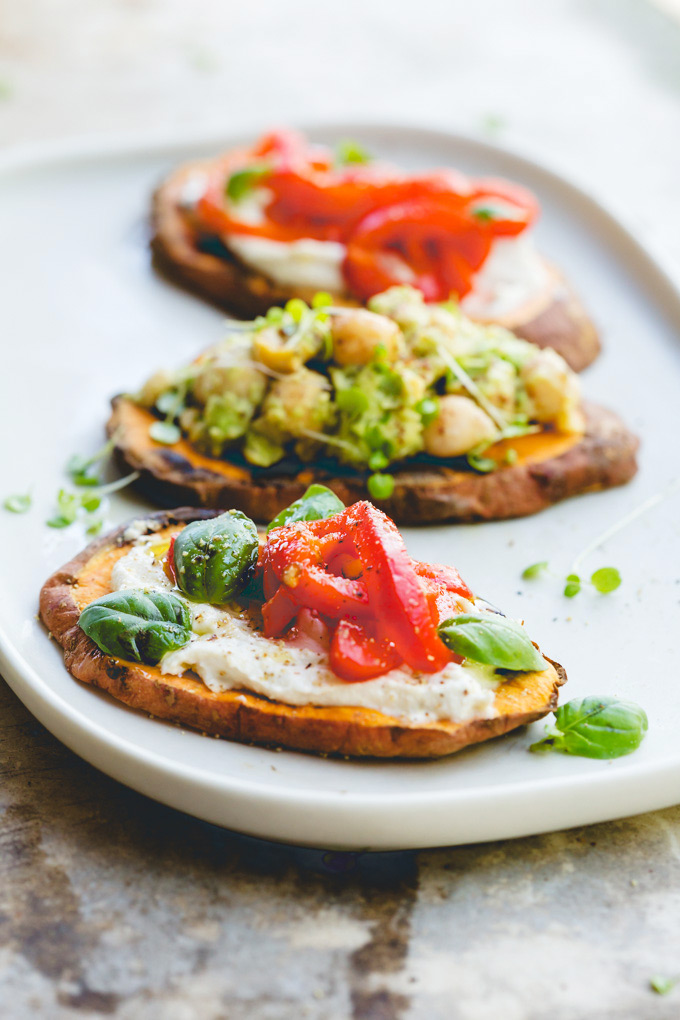 Three serves of sweet potato toast on a rectangle white plate. The first and last toast are topped with cashew cream and roasted peppers with the middle serve has the avocado and chickpea mixture.  
