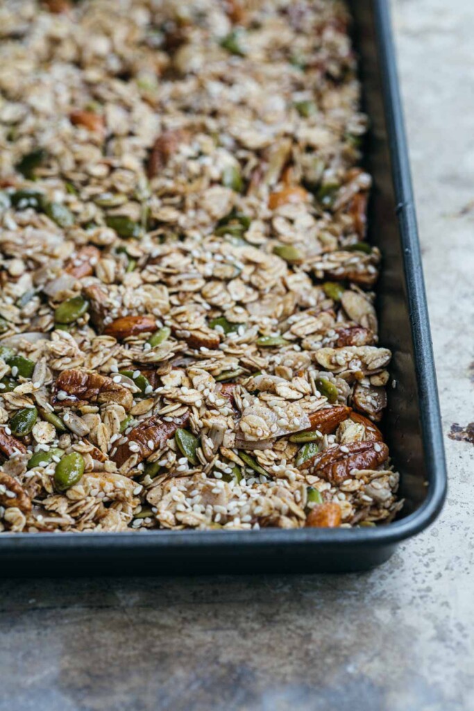 Close-up image of the chunky sesame granola pressed in to the tray before baking. This is a process shot before the granola is cooked to show how muck to push the mixture in to the pan.