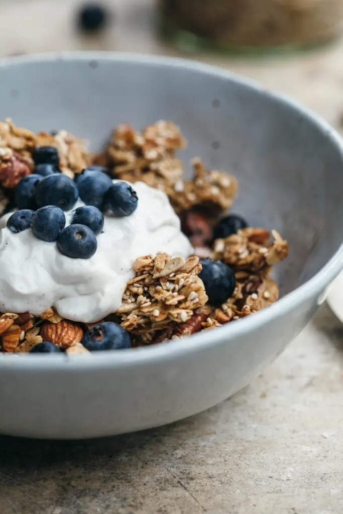 Close up image of chunky sesame granola in a white bowl with coconut yoghurt and blueberries