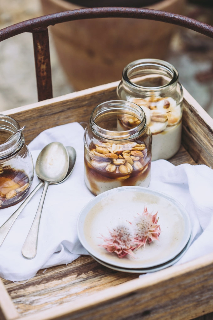 A rustic wooden box resting on a swing seat with three jars of vegan panna cotta, textured napkins and spoons. 