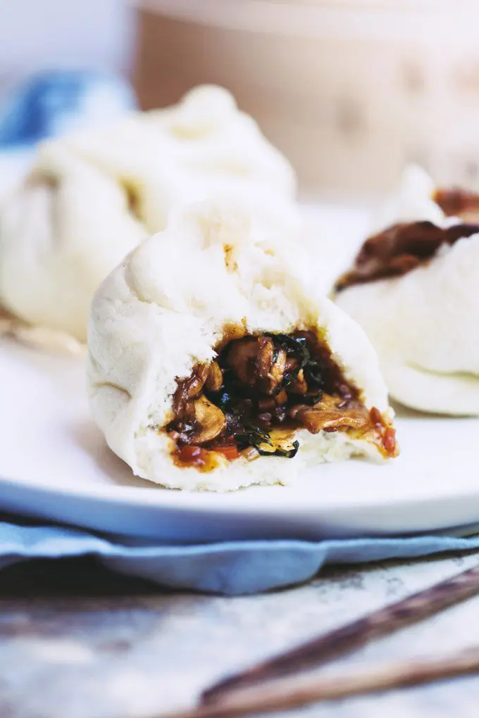 A close-up image of a vegan bao bun with a bite taken out of it on a white plate