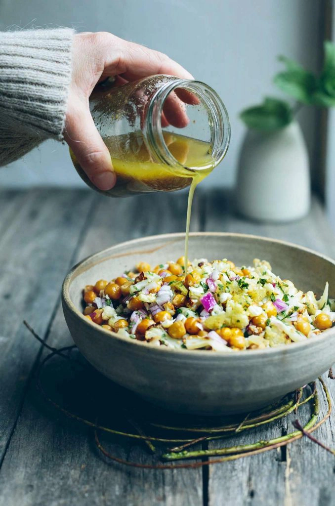 A picture of a woman pouring dressing on a chickpea salad