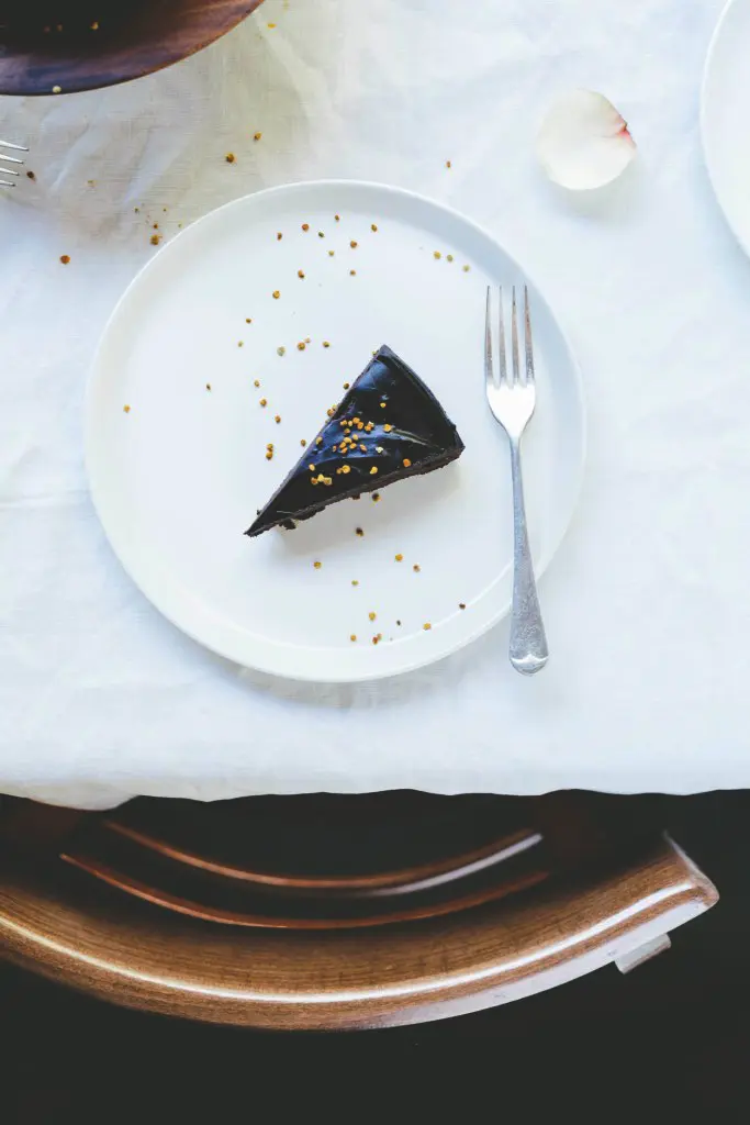 A piece of raw chocolate cake on a white plate on a table with a white cloth