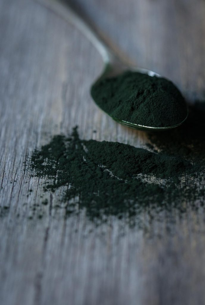 A close up image of a spoon of dark green spirulina powder to show ingredient