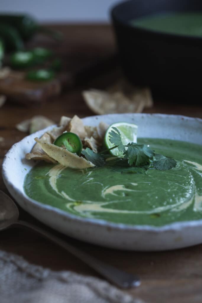 Cheesy Jalapeño Broccoli Soup is a vibrant mix of spicy broccoli soup with a cheesy cashew cream, topped with fresh coriander, lime and corn chips. (v)