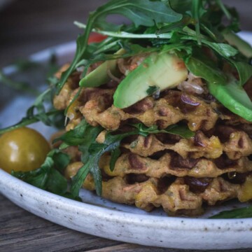 A close up image of potato waffles with avocado on greens on a white plate.