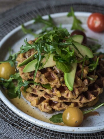 An image of potato waffles with avocado and greens on a white plate.