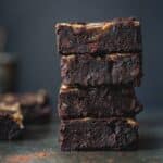 A stack of black bean brownie squares with caramel in front of a blue background.