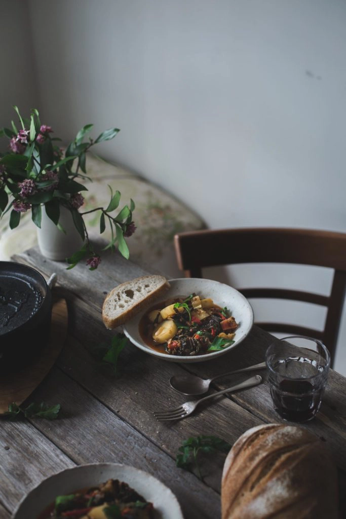 A bowl of potato and lentil stew on a wooden table with a chair in the background. 