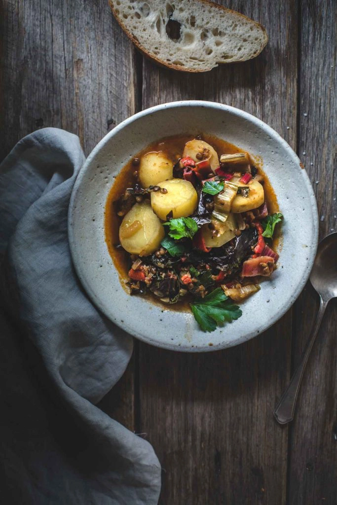 An overhead image of a potato and lentil stew in a rustic white bowl with a napkin. 