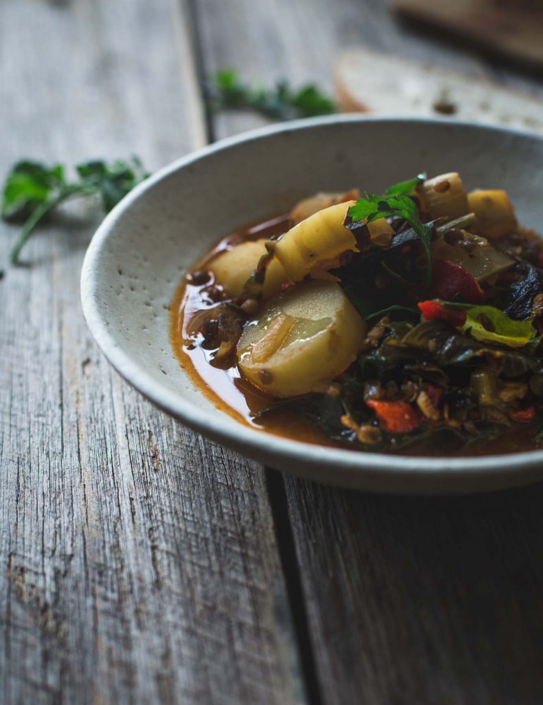 A close up image of a potato and lentil stew in a rustic white bowl. 