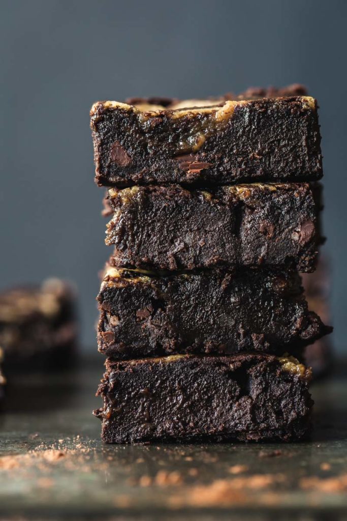 Close-up image of a stack four vegan brownies on a rustic metal tray with cocoa dusted around