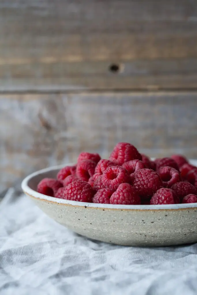 A rustic white bowl of fresh raspberries