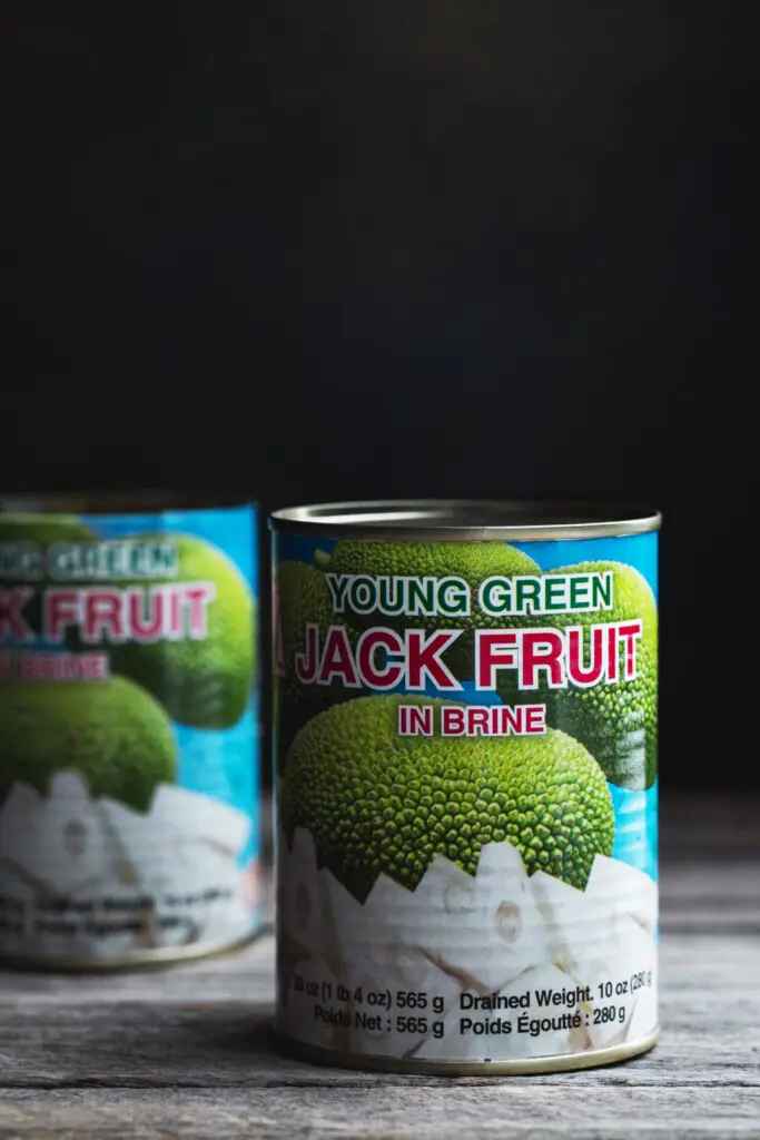 close up image of young jackfruit in cans in a row on a rustic wooden board
