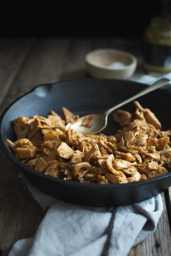 Process image of cooked jackfruit a black iron skillet with a grey cloth underneath.