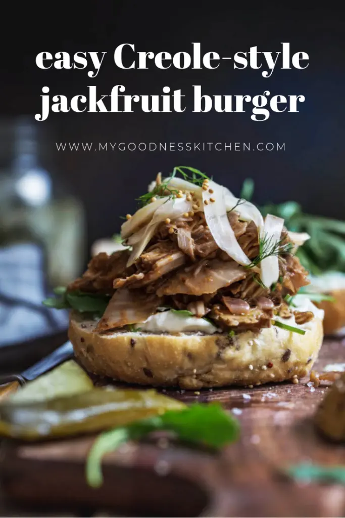 front on image of easy Creole jackfruit burger without it's bun top sitting on a wooden board with pickles in the foreground. Title text overlay in white