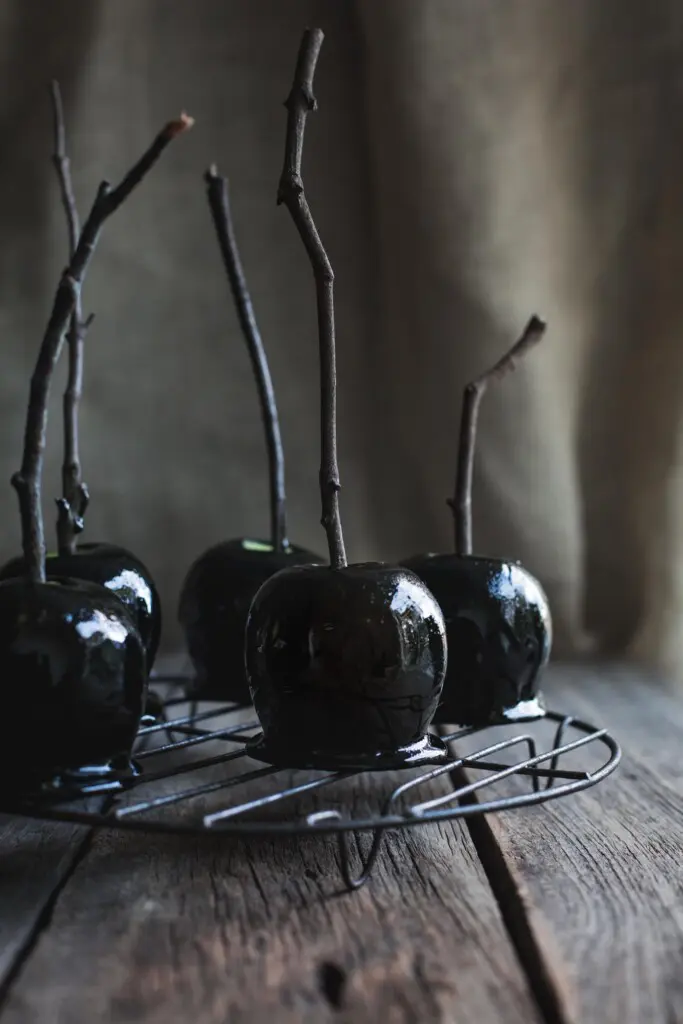 A front on image of 5 Halloween toffee apples with branch handles sitting on a round wire tray