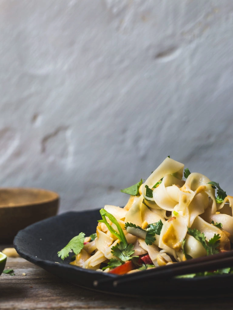 A front on image of Asian noodles on a black plate on a wooden bench. 