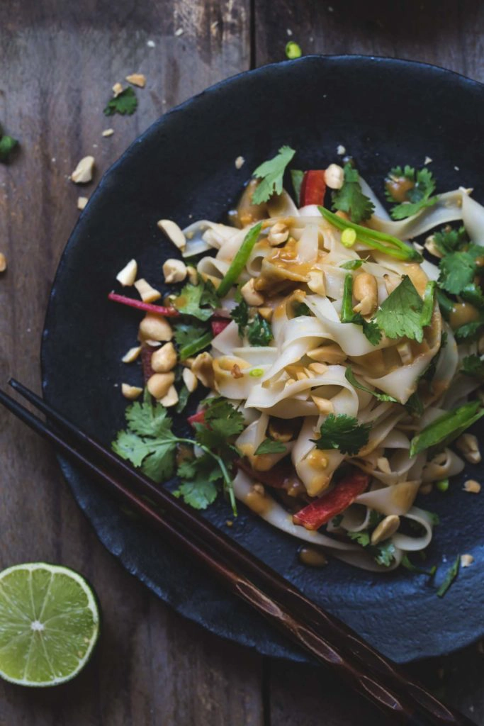 An overhead image of Asian noodles on a black plate with chopsticks.