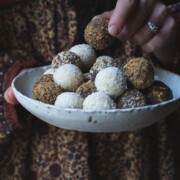 A woman's hand picking up a chocolate truffle from a bowl.