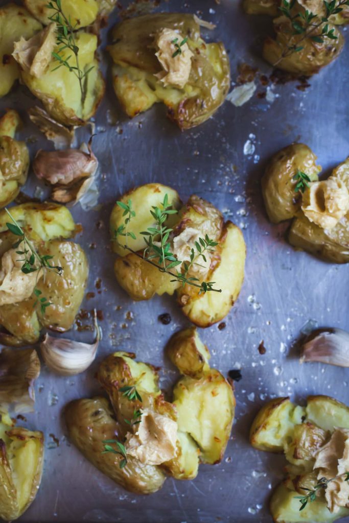 A close-up overhead image of a tray of golden roasted smashed potatoes with sprigs of thyme and miso butter 