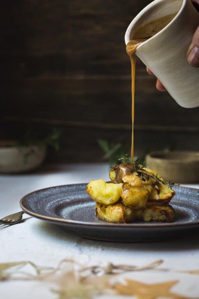 Front on image of a man's hand pouring vegan gravy over a stack of smashed potatoes.