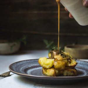 A plate of roast potatoes with gravy being poured.