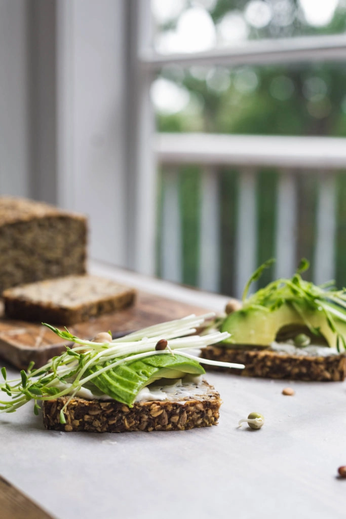 Slices of vegan seeded pumpkin toast topped with mayonnaise and avocado on a wooden board