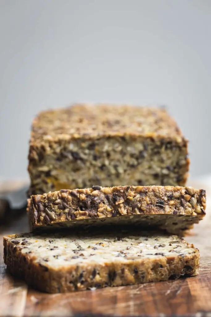 A loaf of seeded pumpkin toast sliced on a wooden board