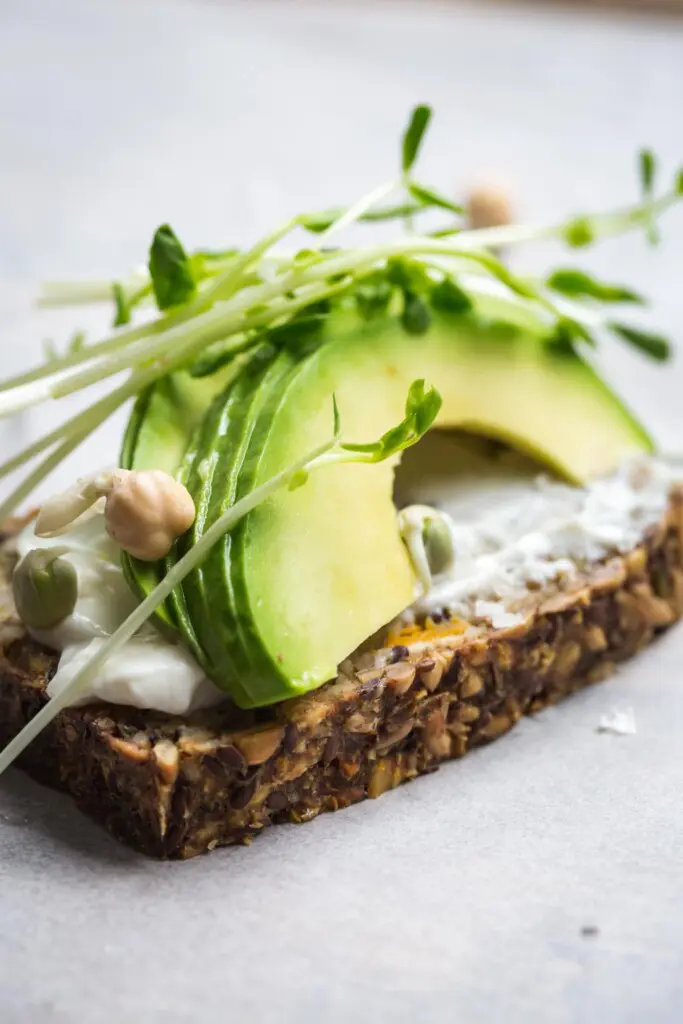 A close up image of seeded pumpkin toast topped with mayonnaise and sliced avocado