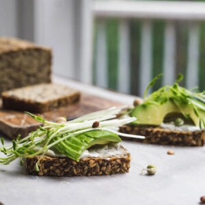 Sliced seeded bread topped with avocado and greens on a white background.