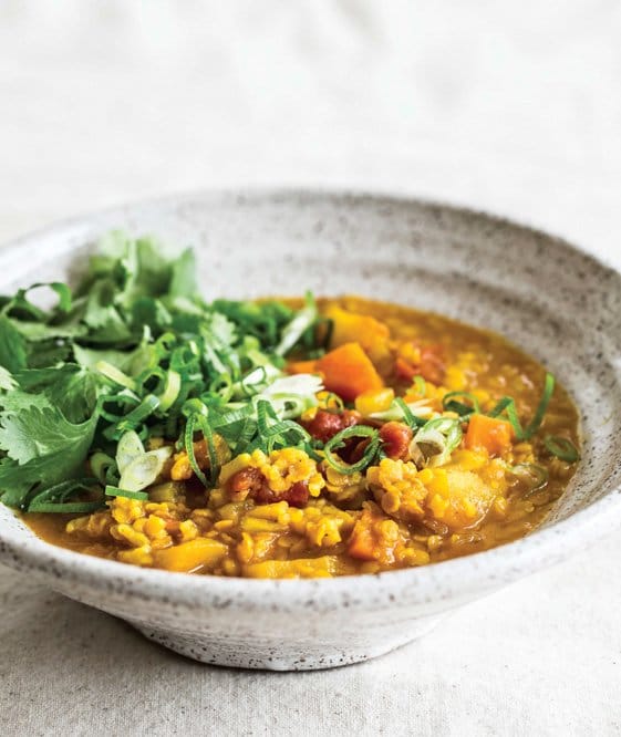 A rustic cream bowl of curry with fresh greens. 