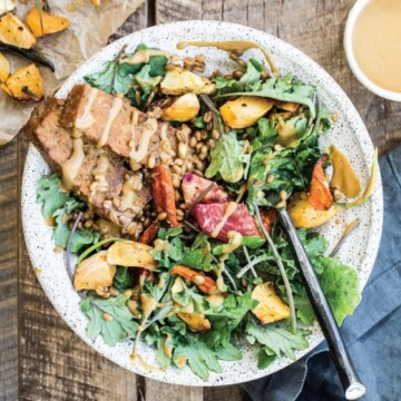 An overhead image of a green salad with tempeh in a white bowl.