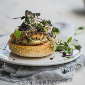 An open cauliflower burger with greens sitting on a plate and grey napkin.