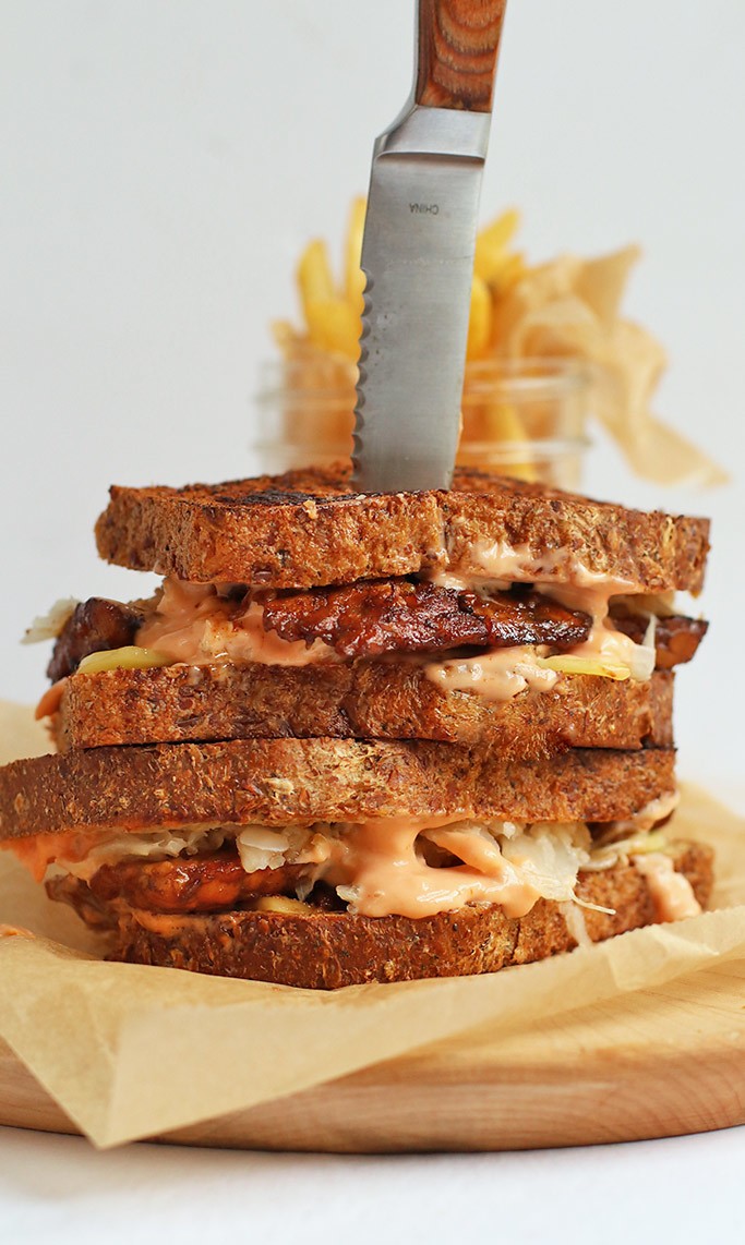 A stacked vegan tempeh rueben sandwich with a steak knife