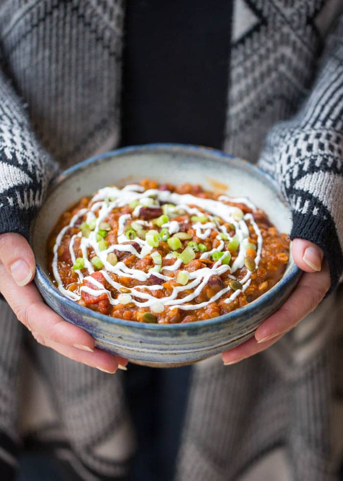 A woman holding a bowl of pumpkin red lentil chilli