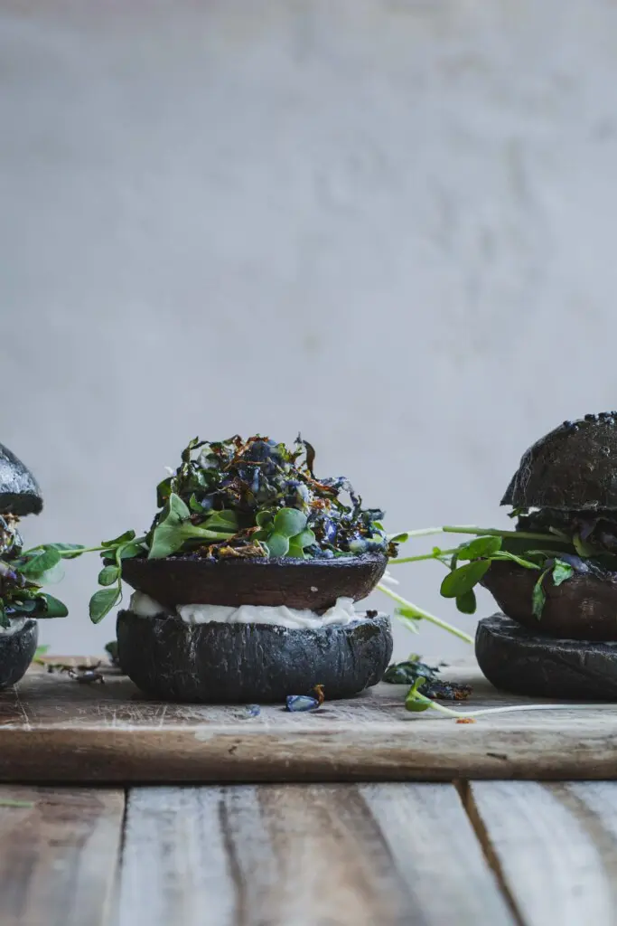 Three Portobello Mushroom Burgers in a horizontal line with the middle burger in focus and it's top bun removed. 