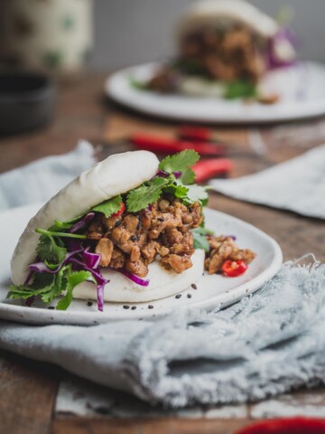 A close up image of a bao bun filled with temper and greens.
