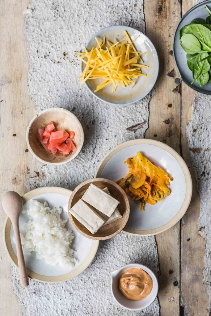 flat-lay image of vegan crispy tofu sushi burrito ingredients laid out on plates on a distressed white board